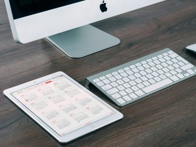 A sleek and modern office desk setup featuring an iMac, iPad with calendar, keyboard, and mouse.